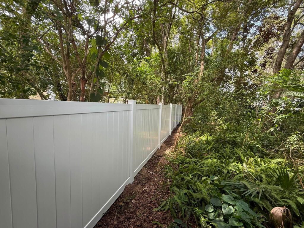 White vinyl privacy fence installed along a wooded residential property line
