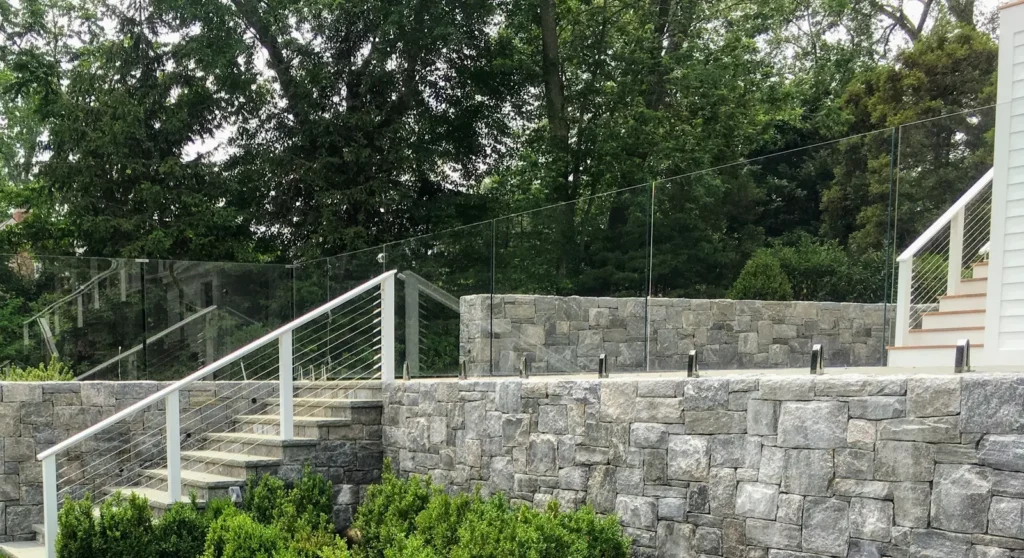 Exterior glass railing mounted above a stone terrace wall beside outdoor stairs