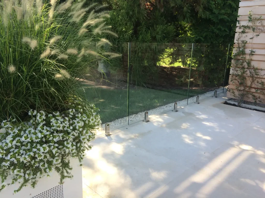 Clear frameless glass safety fence beside a landscaped residential patio