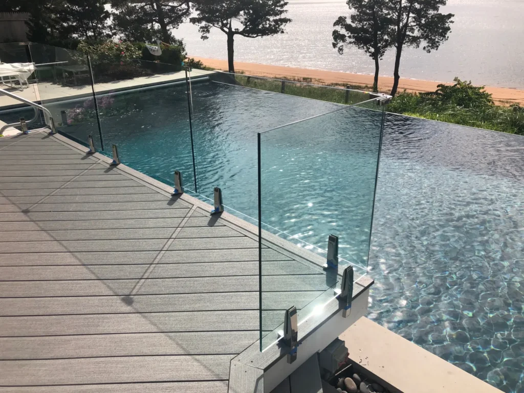 Frameless glass pool fence installed on a wood deck beside the swimming pool