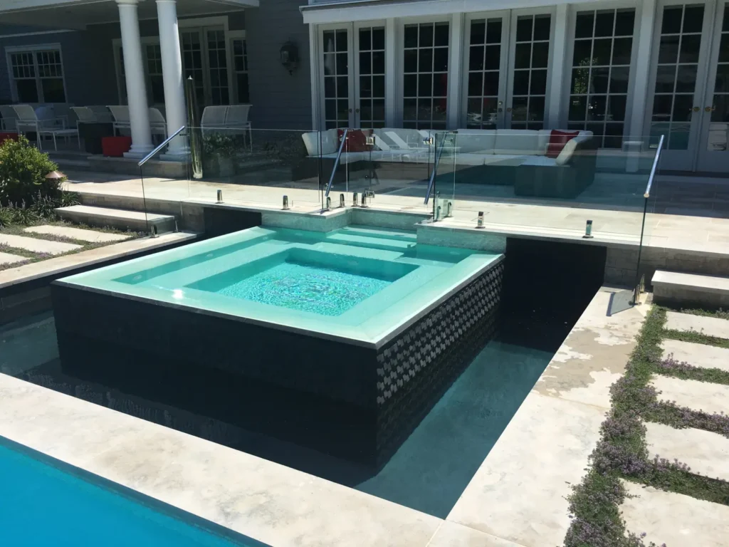 Frameless glass safety enclosure surrounding a raised spa and pool deck